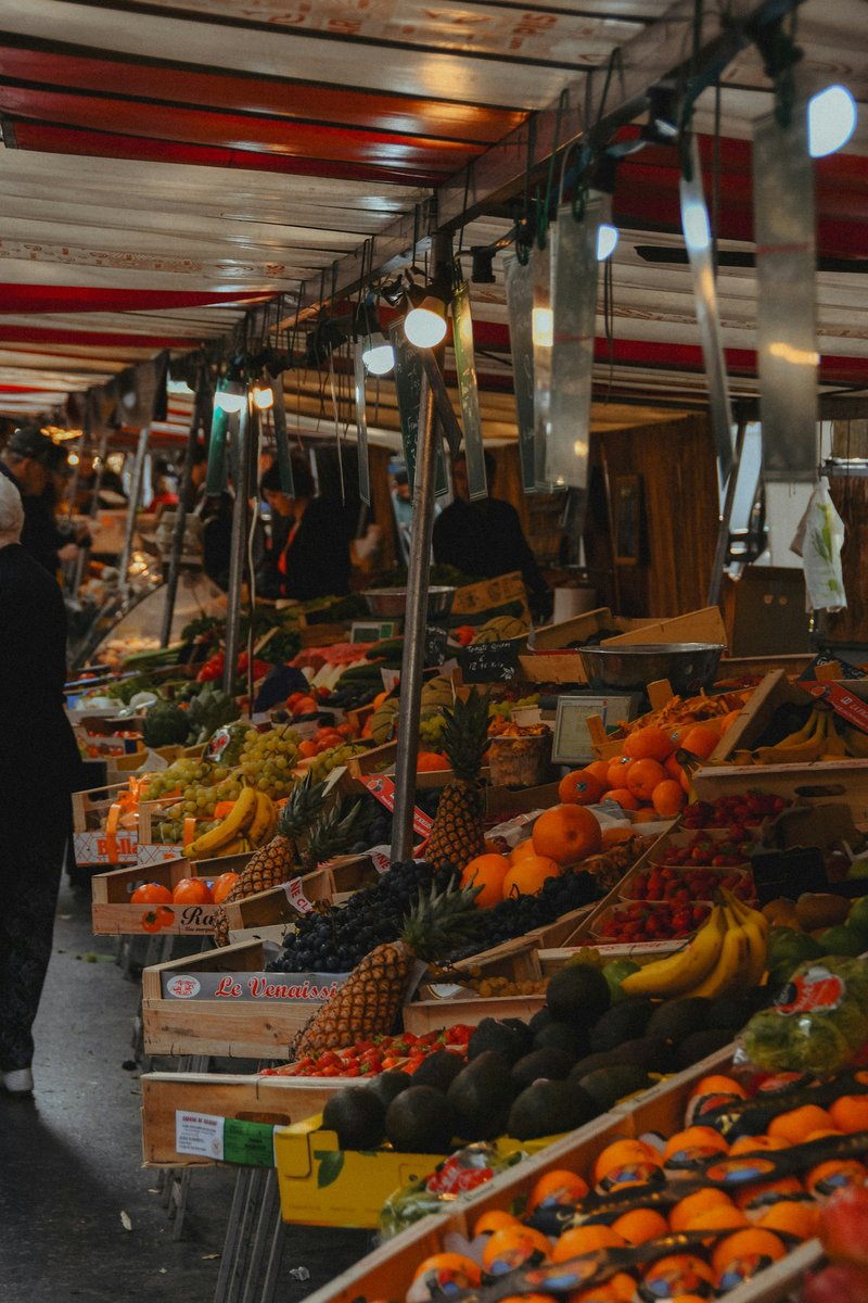 Allée d'un marché couvert bordée d'étals de fruits et légumes