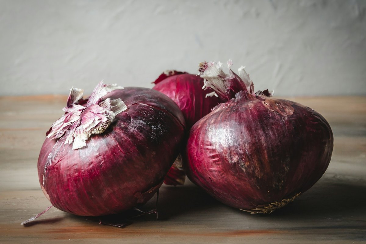 Trois oignons rouges posés sur une table en bois